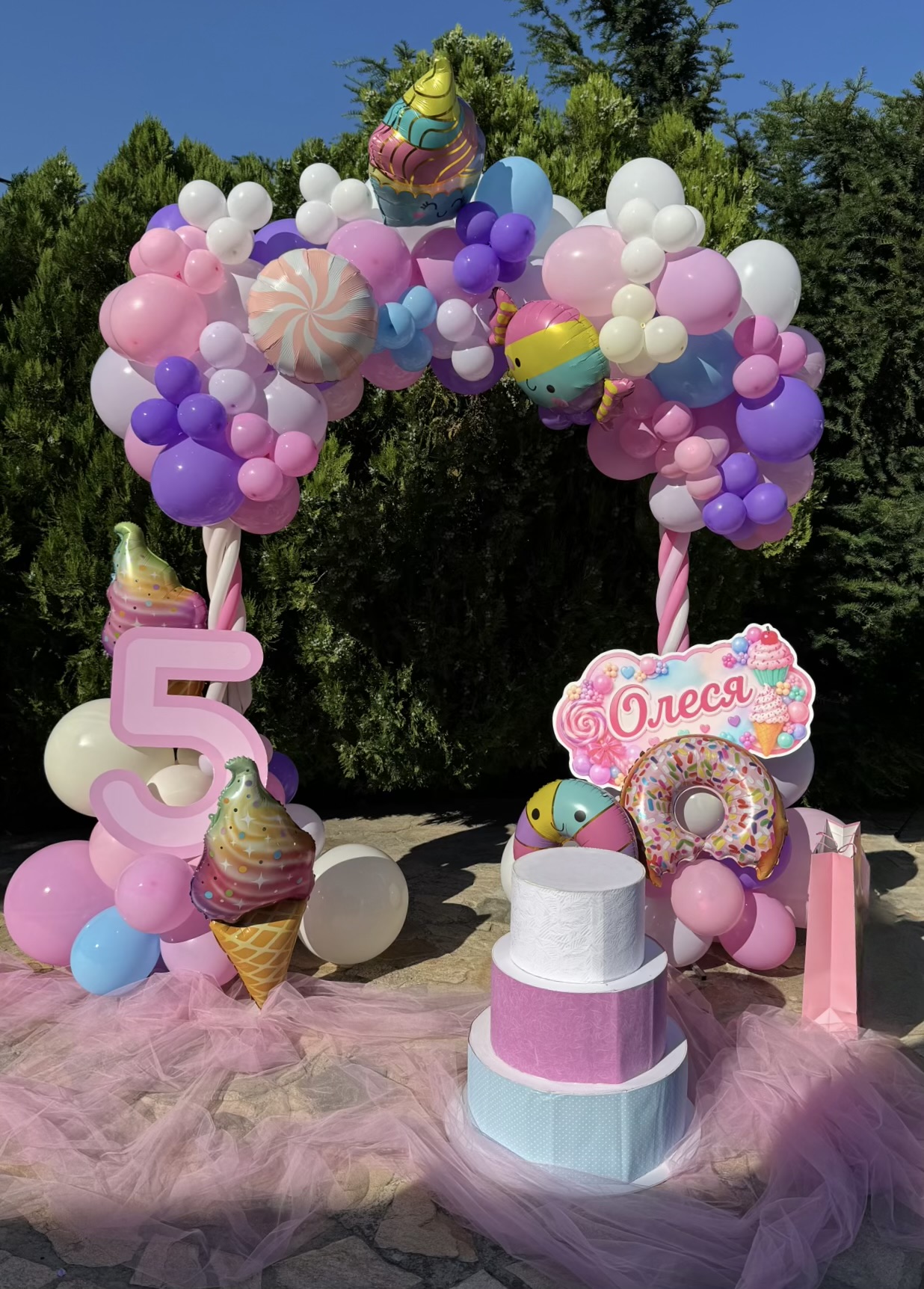 Candy themed birthday balloon arch with pastel balloons, cake stand, and custom name sign