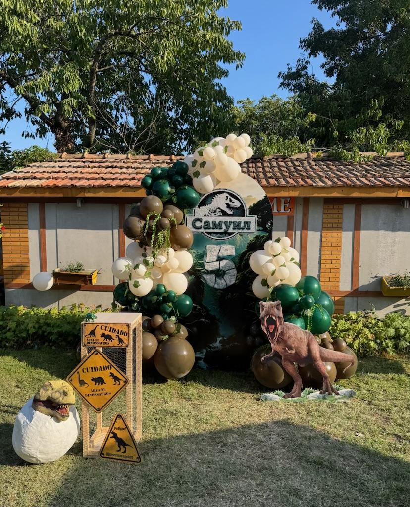 Dinosaur themed fifth birthday setup with green, cream, and brown balloon decor