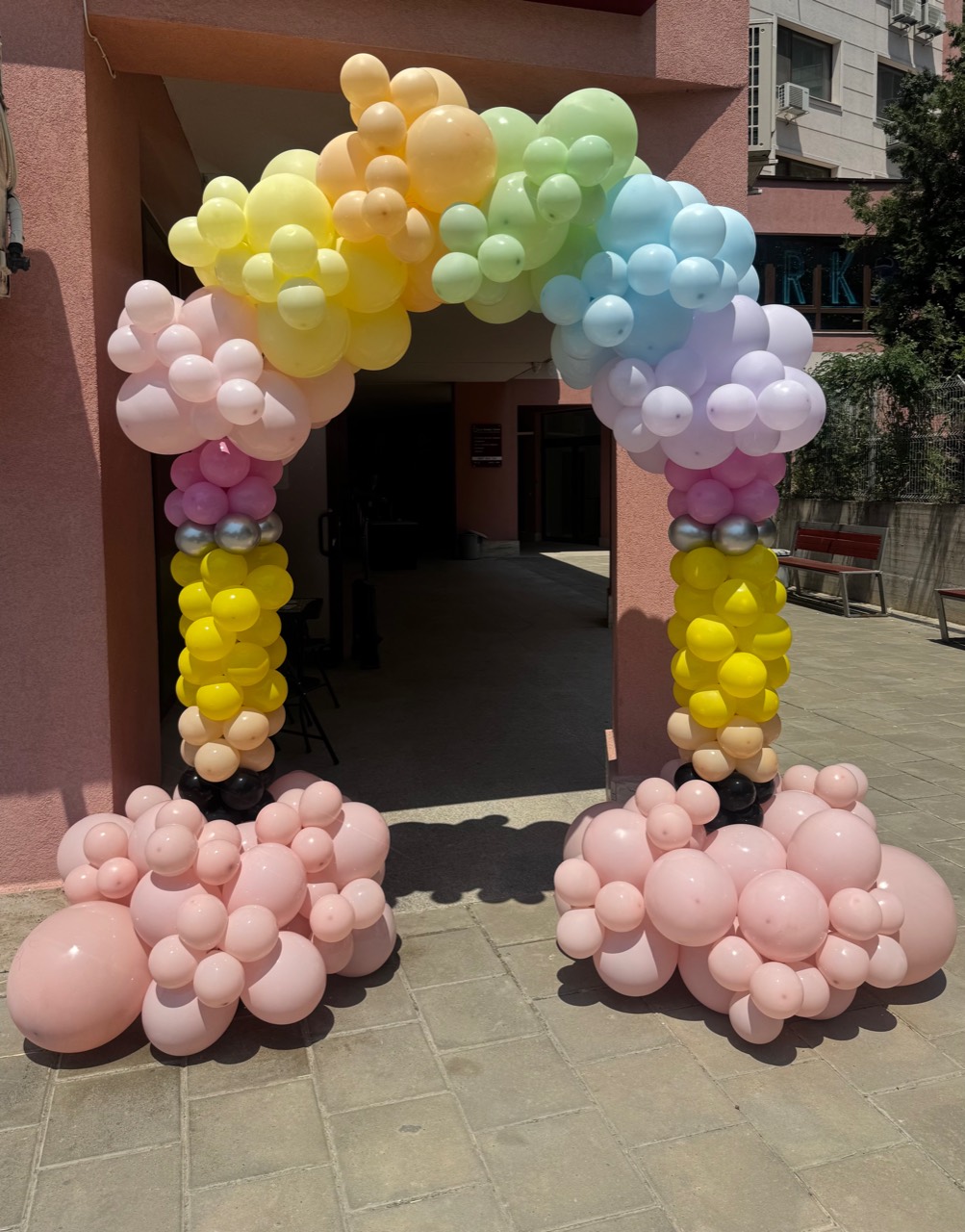 Pastel rainbow balloon arch with pink balloon bases for a children's celebration